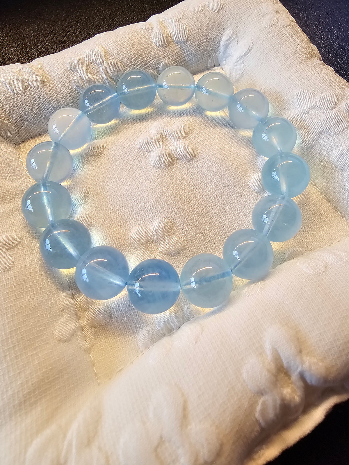 Aquamarine Bracelet. A beaded bracelet made of translucent light blue round beads, displayed on a textured white fabric cushion.